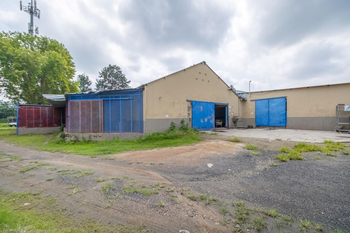 Industrial property exterior featuring large sliding access doors, concrete yard area, and metal structural enclosures under a cloudy sky.