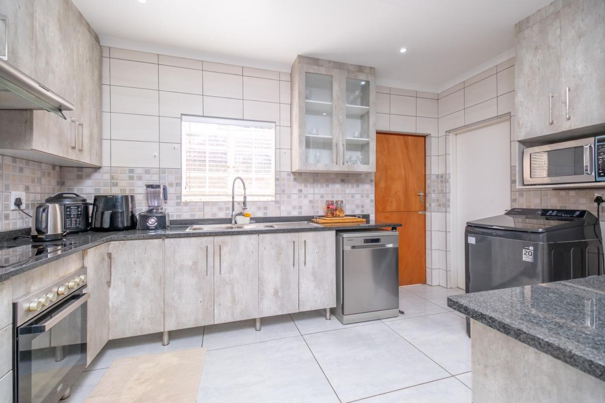 Modern kitchen featuring light wood-grain cabinetry, granite countertops, tiled splashbacks, built-in oven, extractor fan, and integrated space for appliances.