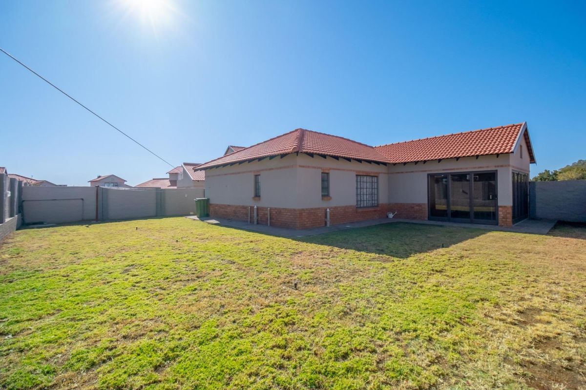 A view of the rear exterior of the house featuring a tiled roof, brick base detailing, and a spacious private garden area.