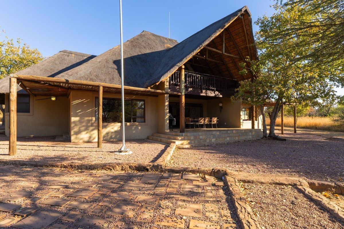 A spacious house featuring a traditional thatched roof, a covered patio area, and a natural gravel and paved exterior setting.