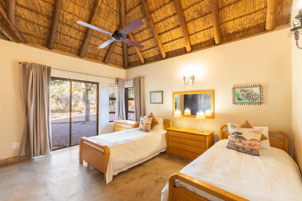 A spacious bedroom featuring a high vaulted thatched ceiling, exposed timber beams, a ceiling fan, and sliding glass doors leading to the outdoors.