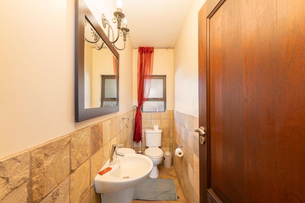 A compact guest bathroom featuring stone-tiled walls, a pedestal basin, and a standard toilet, finished with a wooden door and wall-mounted lighting.