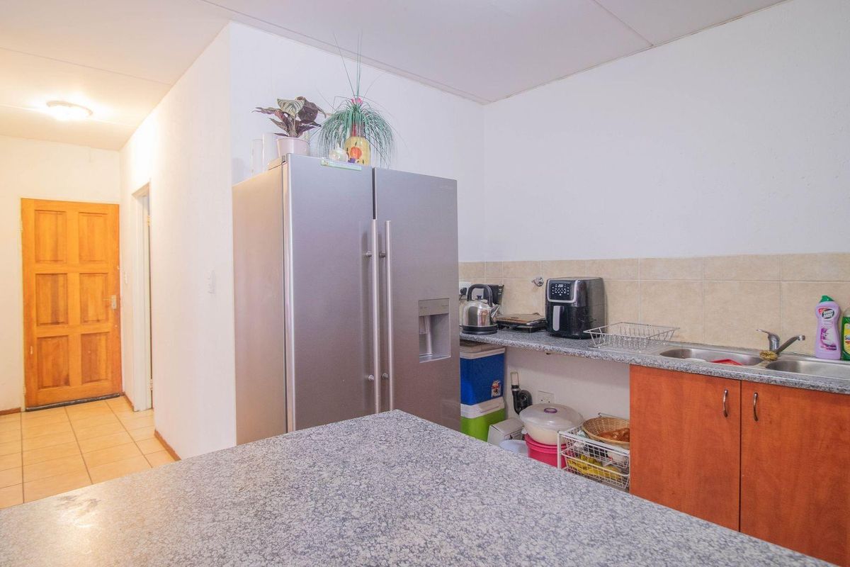A functional kitchen area featuring granite countertops, wooden cabinetry, and a stainless steel sink, with an adjacent hallway leading to a wooden door.