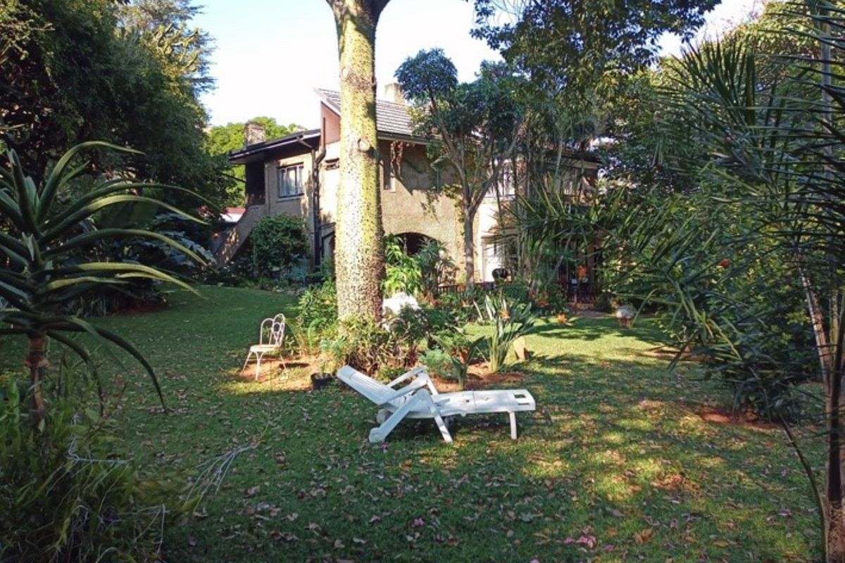 A view of the rear garden and backyard area featuring mature trees, established landscaping, and a view of the house exterior.