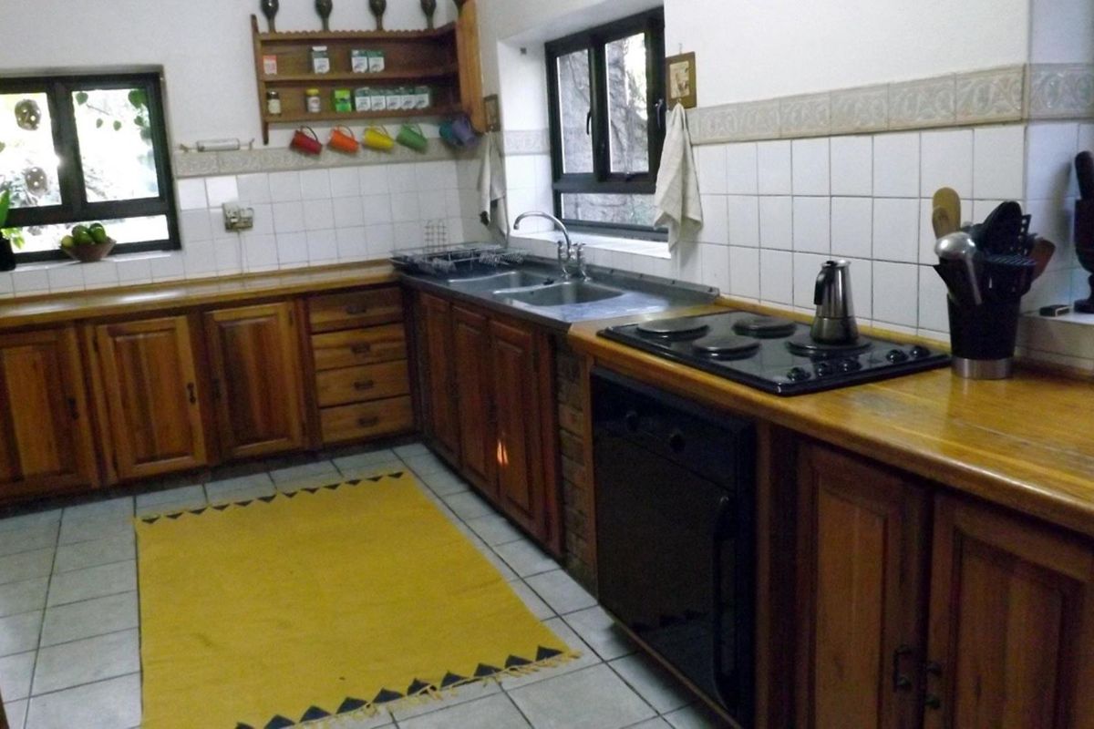 A functional kitchen featuring wooden cabinetry, tiled flooring, a built-in electric hob and oven, and a double-basin sink with tiled splashbacks.