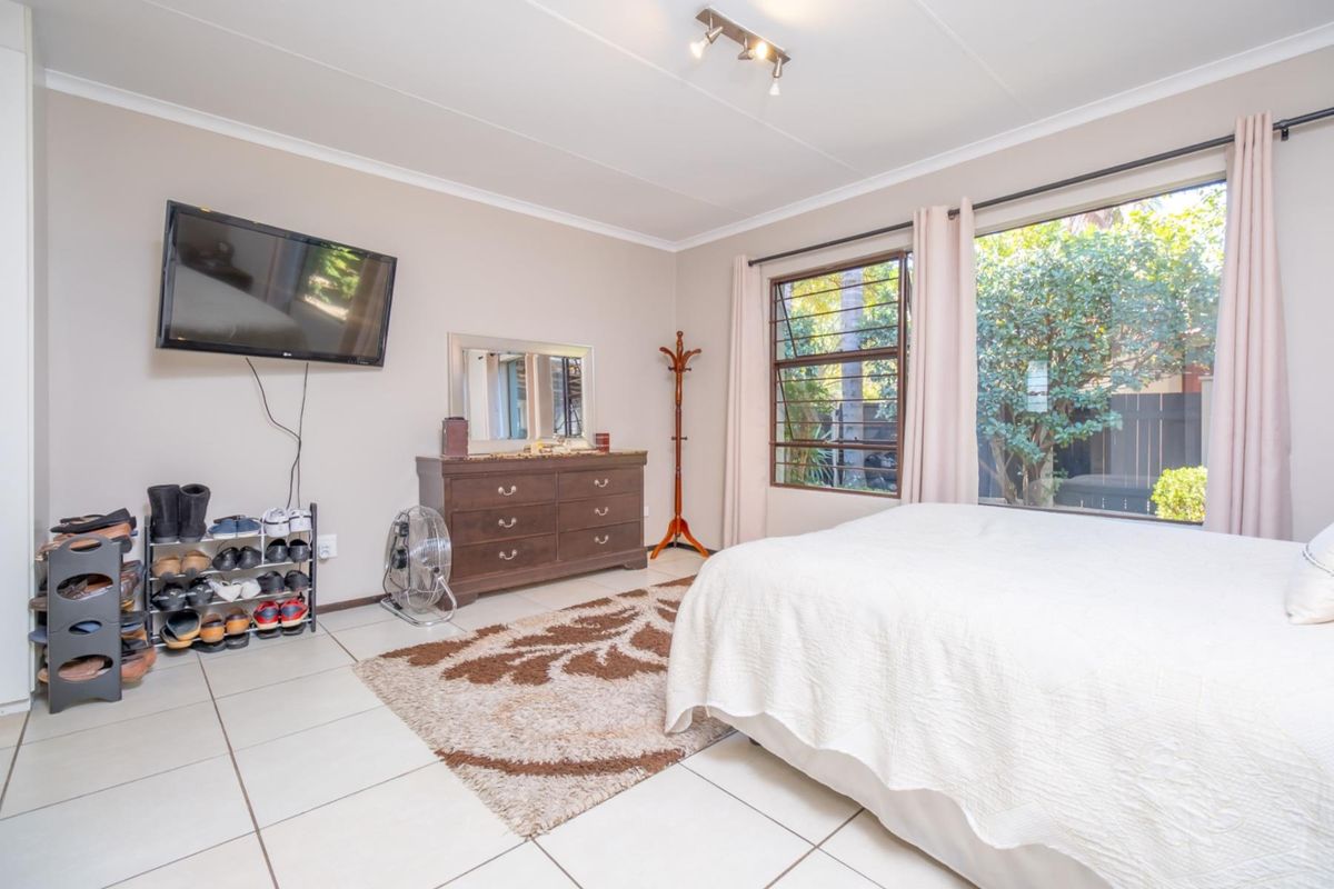 A well-lit bedroom featuring tiled flooring, large windows with garden views, and neutral wall finishes.