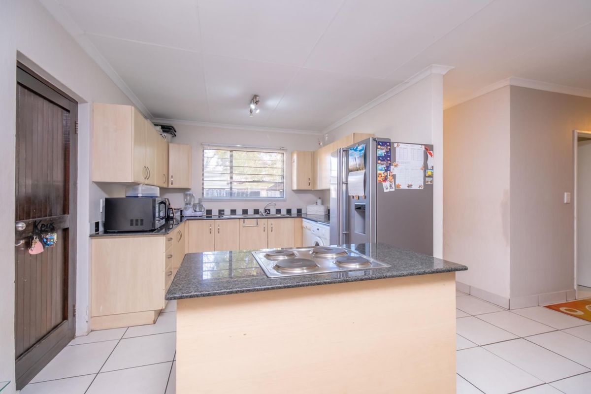 Functional kitchen featuring light wood cabinetry, granite countertops, a central island with a built-in electric hob, and tiled flooring throughout.