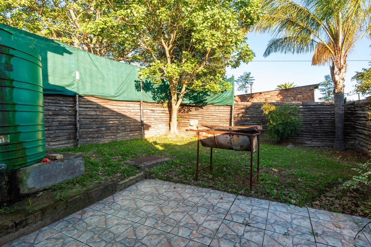A private rear garden area featuring a paved patio, a large green water storage tank, and a rustic timber fence boundary.