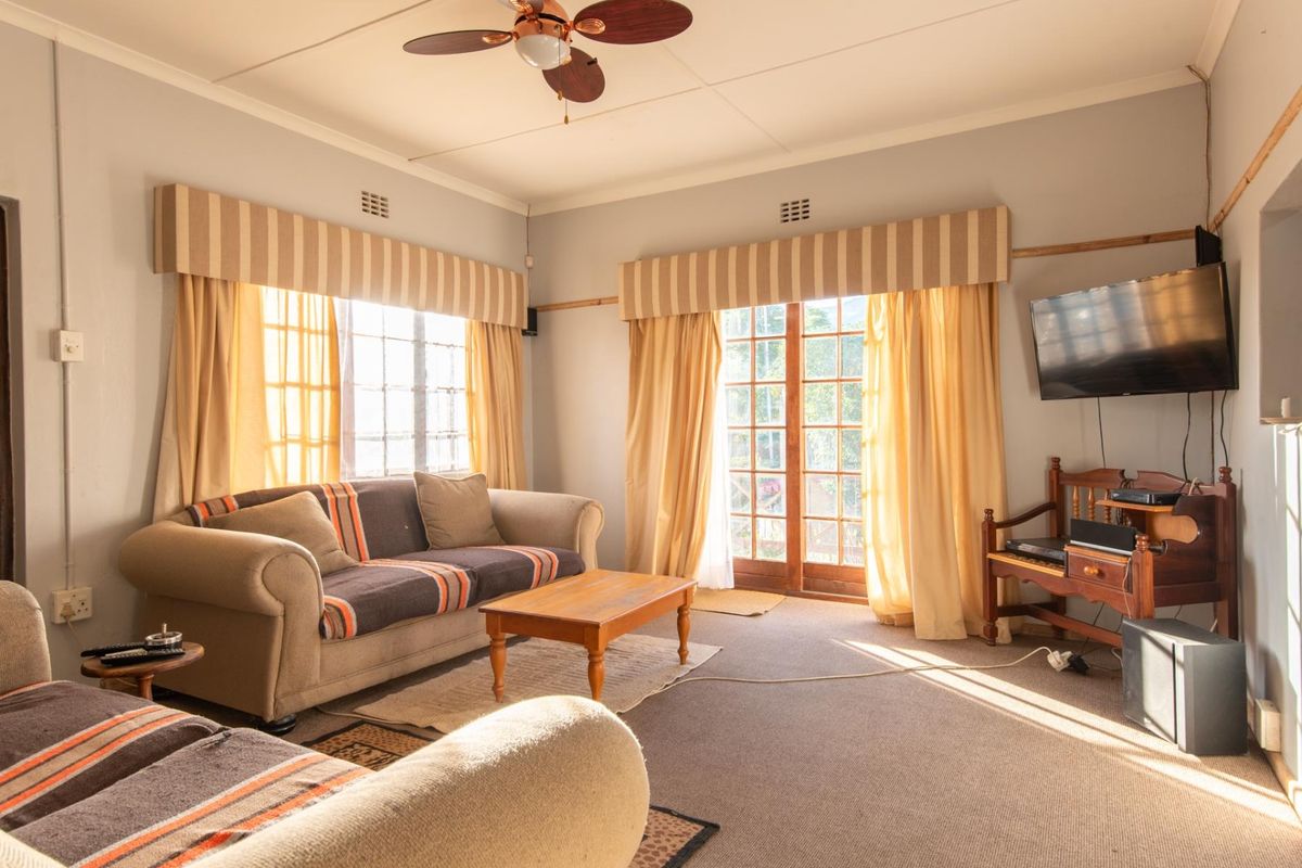 A living room featuring a ceiling fan, large windows, and glass-paneled doors providing natural light and access to the exterior.
