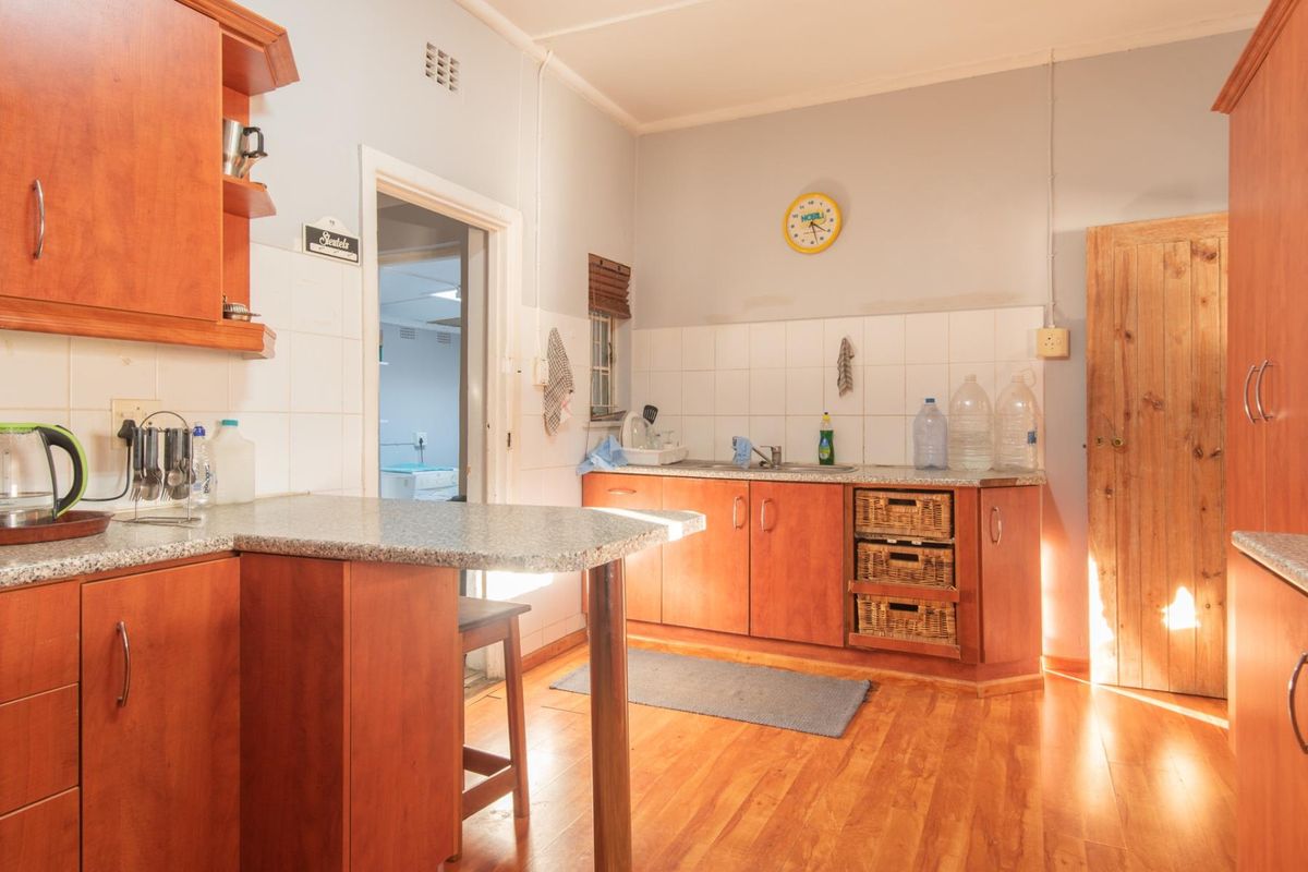 A functional kitchen featuring wooden cabinetry, laminate countertops, and timber flooring, with a breakfast bar and direct access to an adjacent utility room.