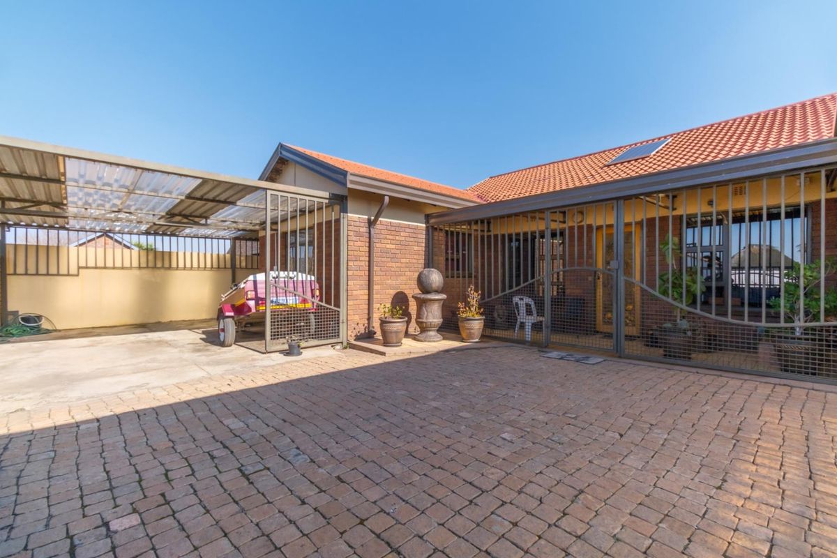 A paved rear courtyard area featuring a covered carport, brick exterior walls, and secure metal gate enclosures.