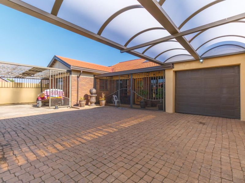 A paved driveway area featuring a covered carport structure, secure metal gates, and a single garage door, providing ample off-street parking.