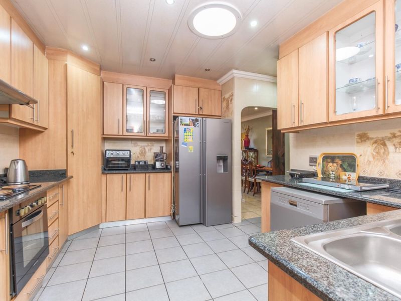 A functional kitchen featuring light wood cabinetry, granite countertops, integrated oven, extractor fan, and tiled flooring with an adjacent dining area.