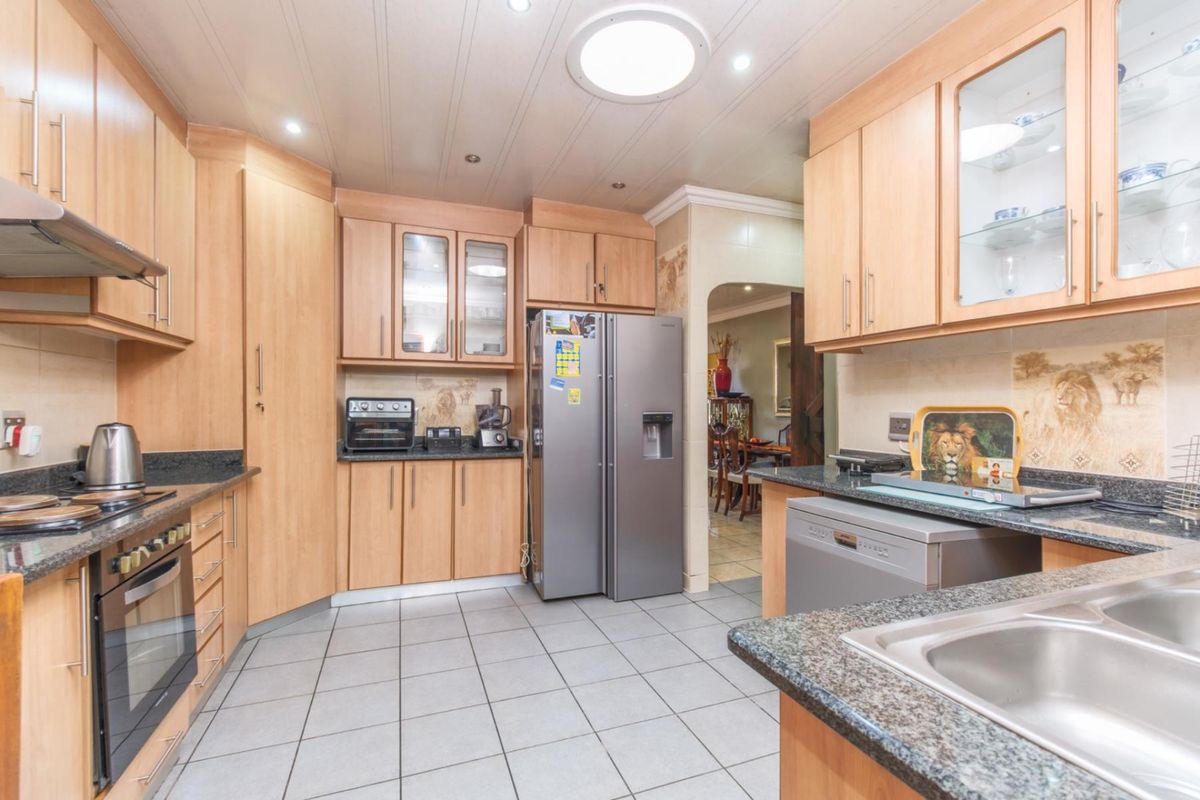 A functional kitchen featuring light wood cabinetry, granite countertops, integrated oven, extractor fan, and tiled flooring with an adjacent dining area.