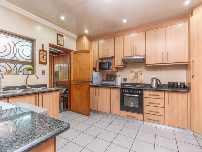 A functional kitchen featuring light wood cabinetry, granite countertops, a built-in oven, extractor fan, and tiled flooring.