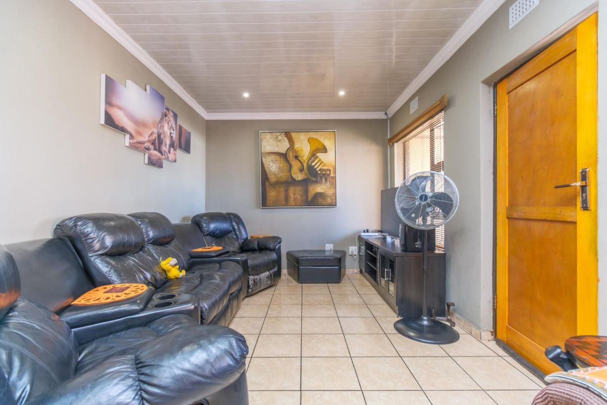 A living room featuring tiled flooring, a glossy panelled ceiling, and a wooden exterior door, providing a functional and comfortable living space.