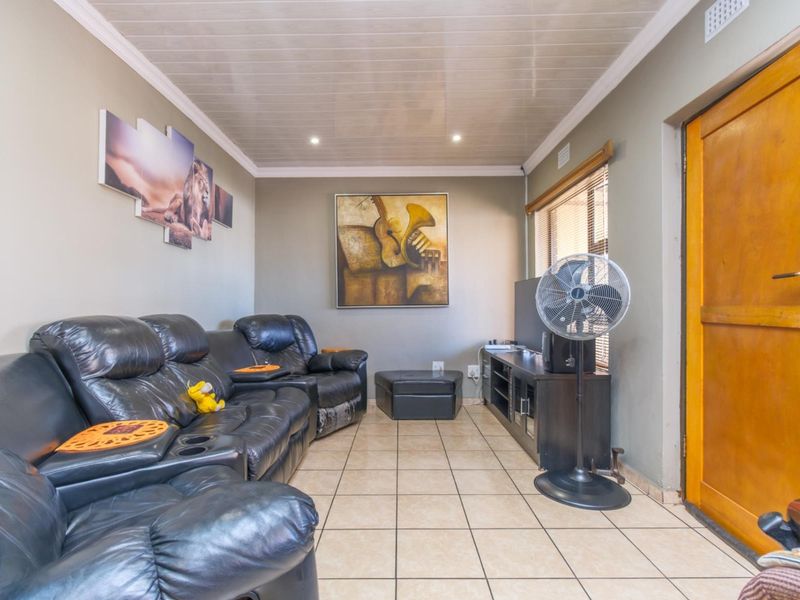 A living room featuring tiled flooring, a glossy panelled ceiling, and a wooden exterior door, providing a functional and comfortable living space.