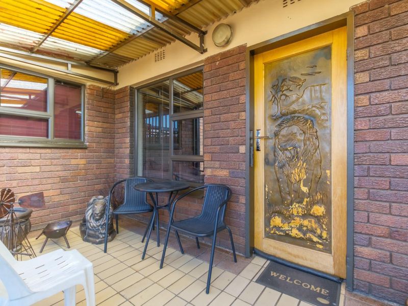 A covered patio entrance featuring face-brick walls, tiled flooring, and a decorative carved wooden front door.