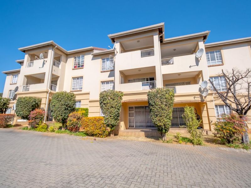 Exterior view of a multi-story apartment complex featuring balconies, paved driveway, and established landscaping.