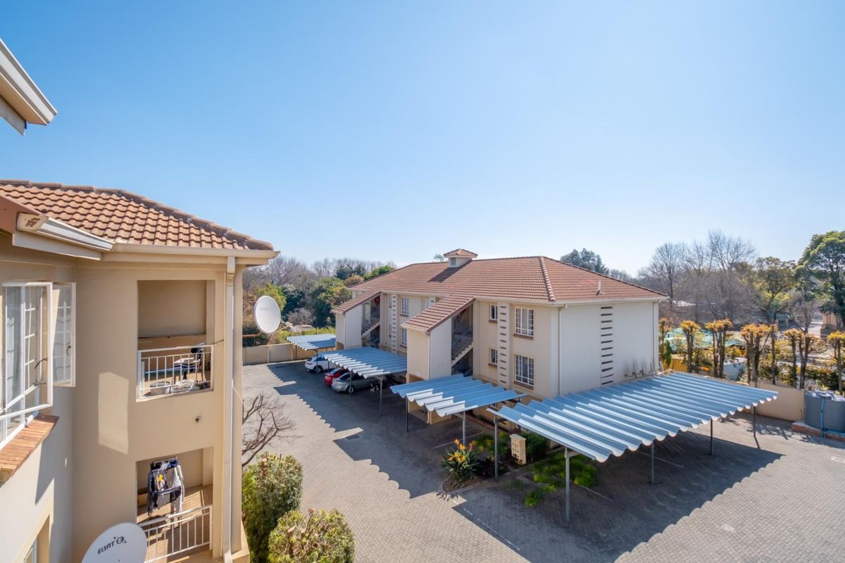 Elevated view of the apartment complex grounds, featuring paved parking areas with covered carports and multi-story residential building blocks.