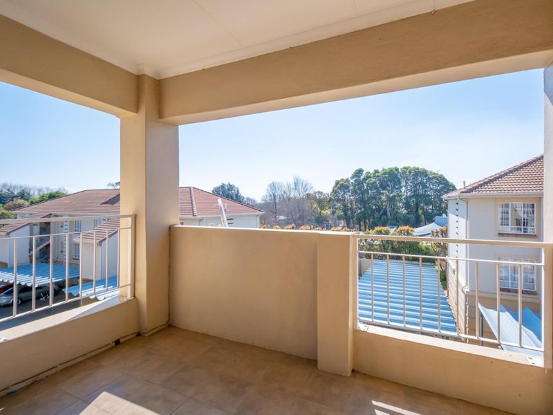 A covered balcony with tiled flooring and metal railings, offering an open view of the surrounding apartment complex and neighborhood.