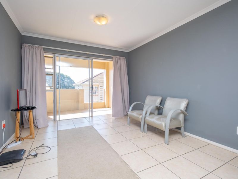 A bright living room featuring tiled flooring, grey painted walls, and sliding glass doors that open onto a private balcony.