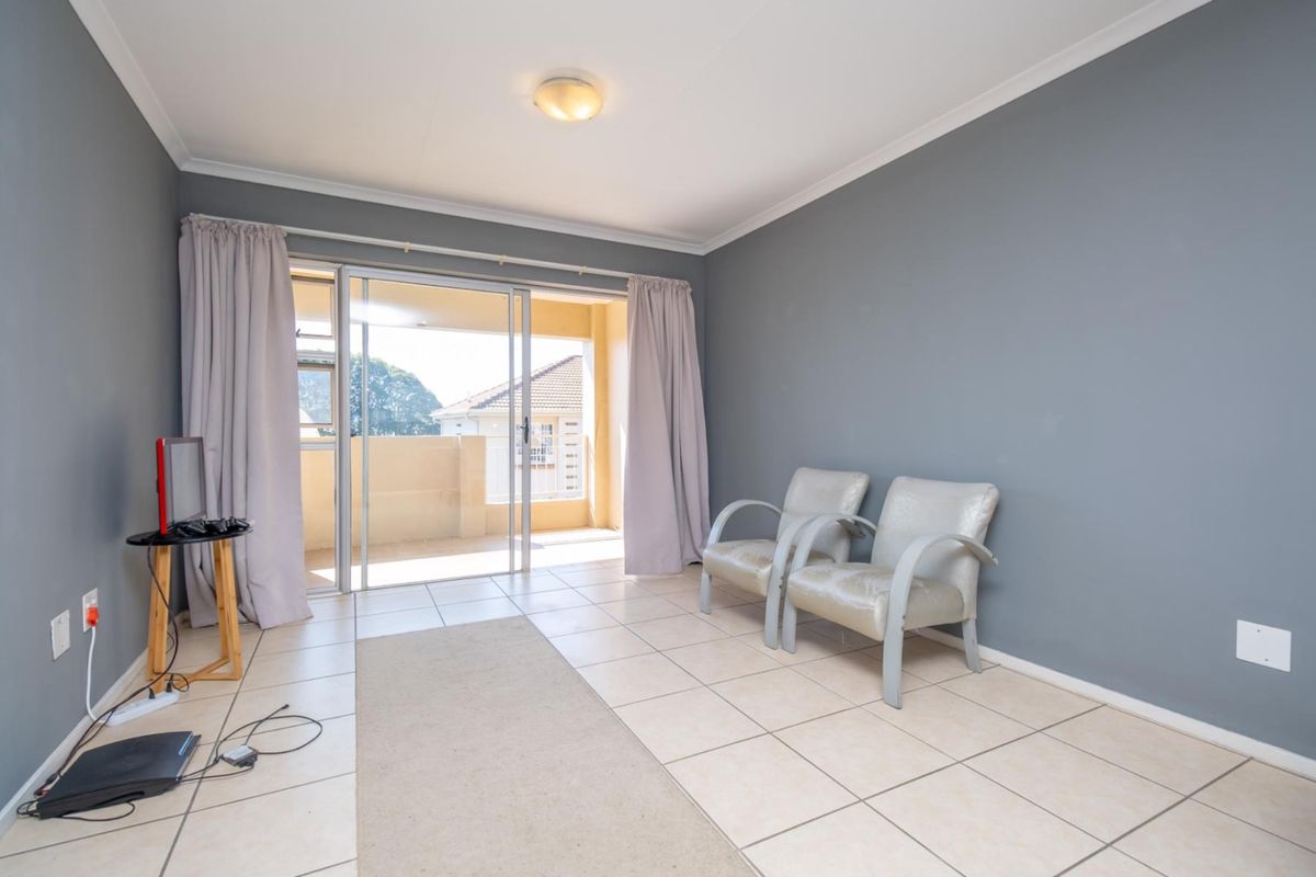 A bright living room featuring tiled flooring, grey painted walls, and sliding glass doors that open onto a private balcony.