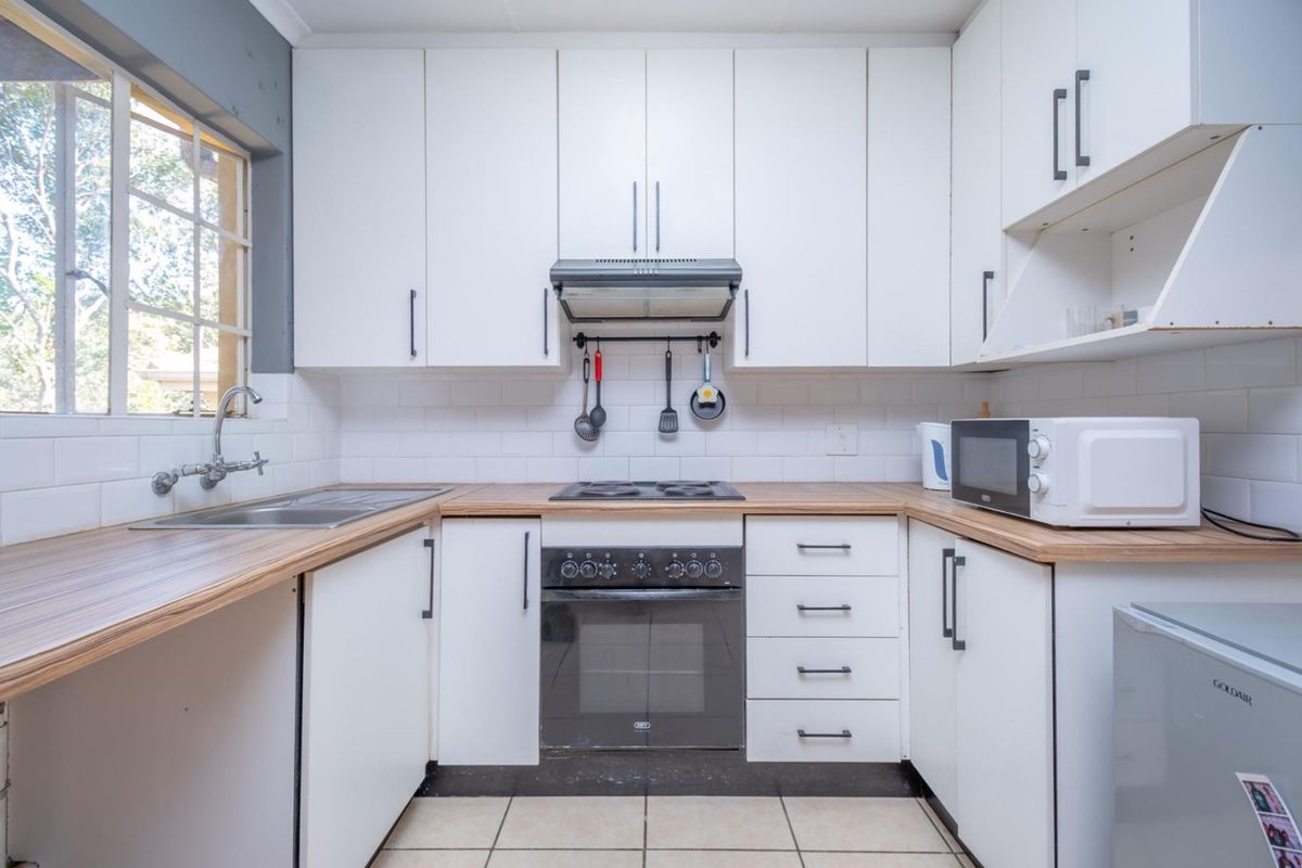 A functional kitchen featuring white cabinetry, wood-look laminate countertops, a built-in oven with extractor fan, and a stainless steel sink.