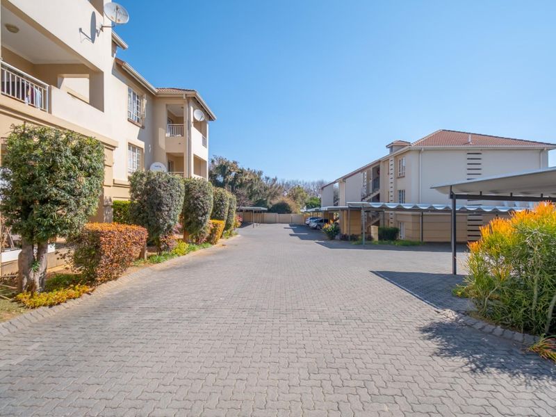 A view of the apartment complex driveway featuring paved surfaces, covered parking bays, and landscaped garden beds alongside the residential buildings.