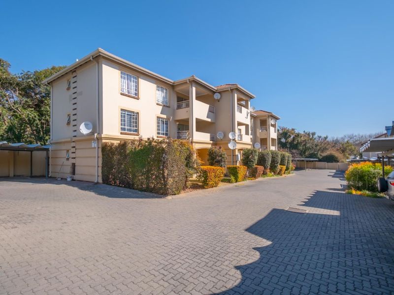 Exterior view of a multi-story apartment complex featuring paved parking areas, covered carports, and landscaped garden borders.
