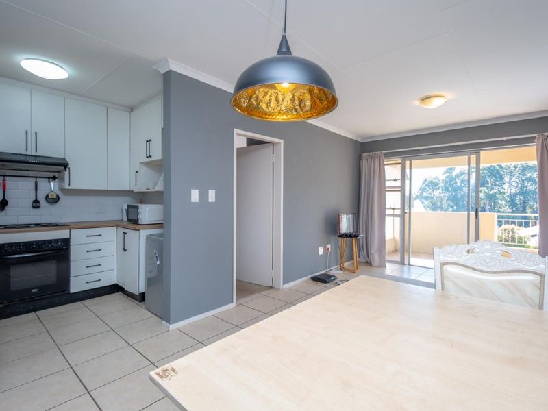 Open-plan kitchen and living area featuring modern white cabinetry, tiled flooring, and sliding glass doors leading to a private balcony.