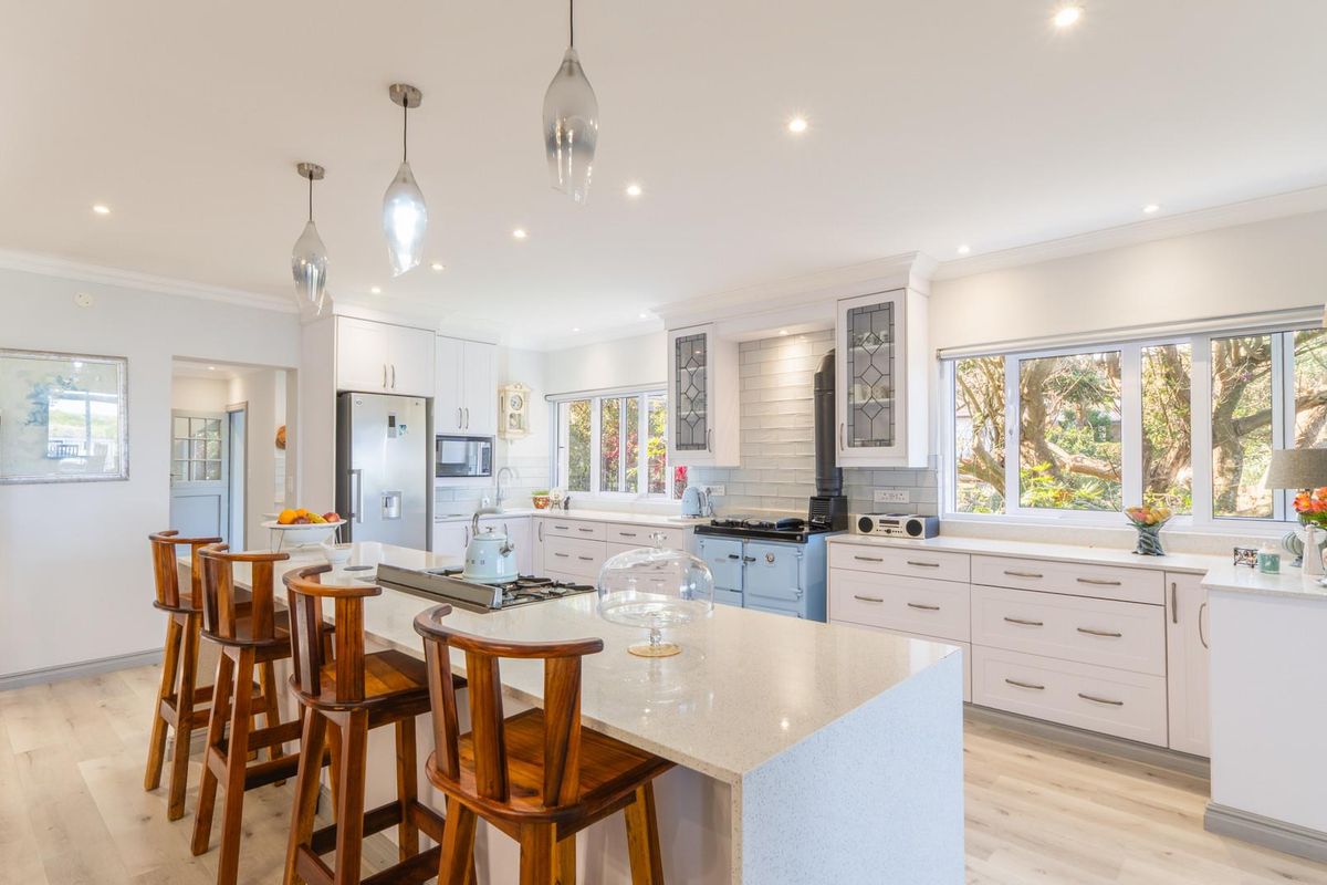 Modern open-plan kitchen featuring a large central island, stone countertops, light cabinetry, and a classic blue range cooker.