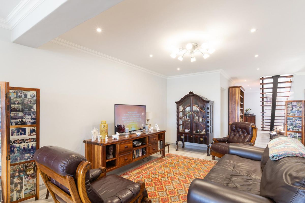 A spacious living room featuring recessed ceiling lighting, crown molding, and an open staircase leading to the upper level.