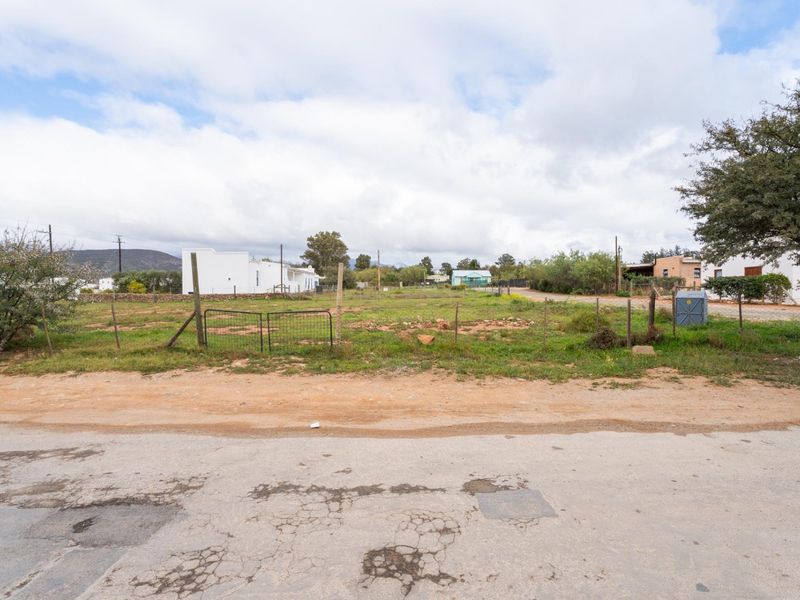 A vacant residential plot of land featuring wire fencing, accessible from an unpaved road, offering a clear space for potential development.