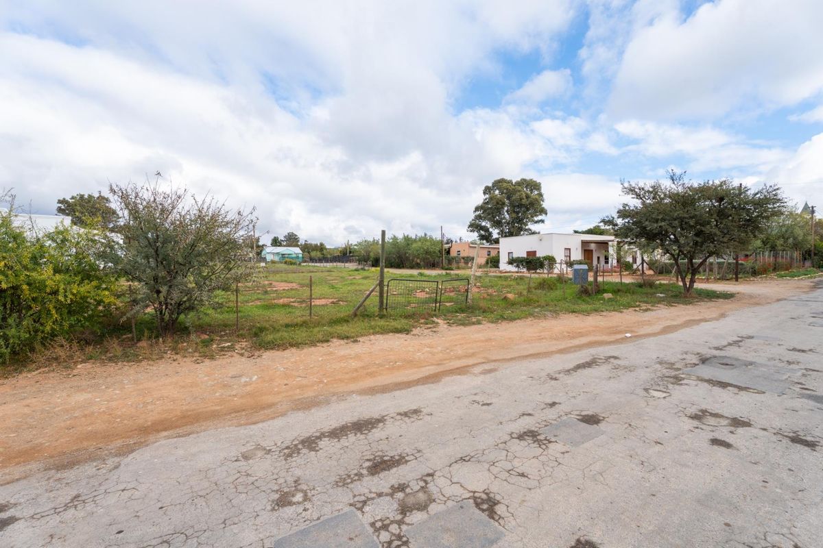 A view of a vacant residential plot from the street, featuring natural vegetation, wire fencing, and surrounding neighborhood context.