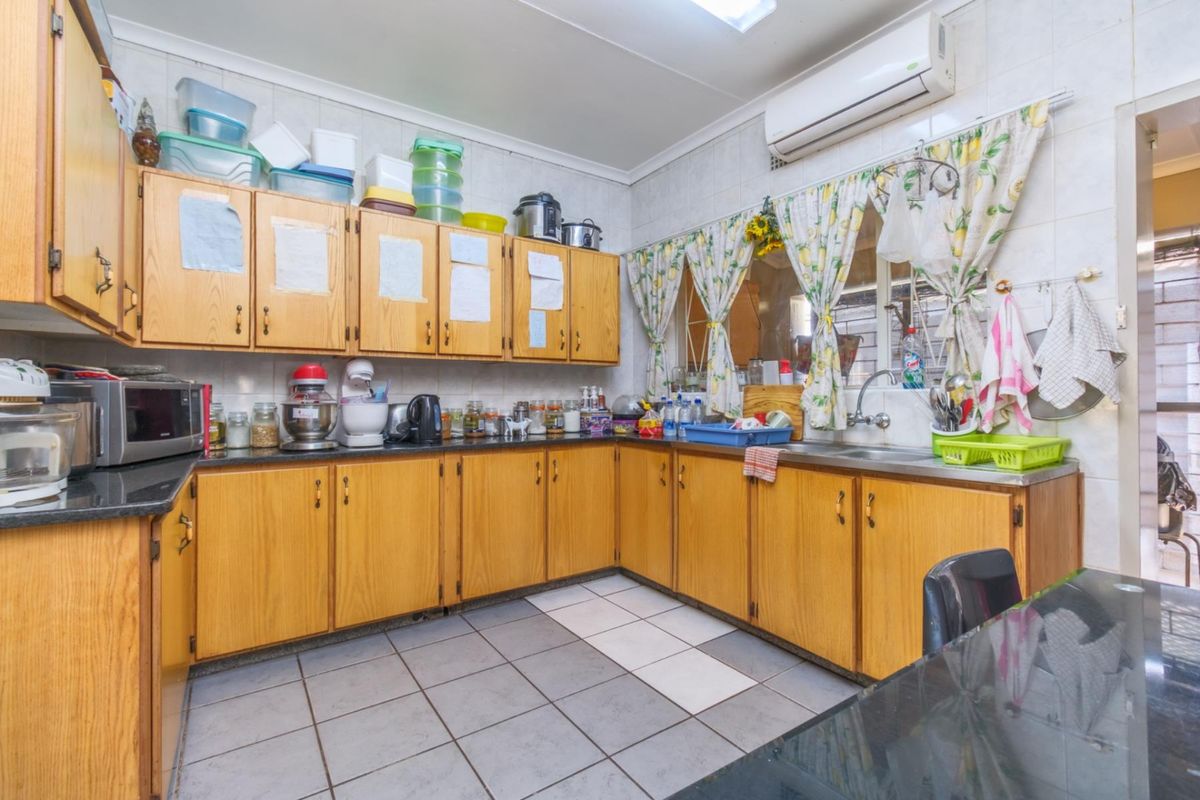 A functional kitchen featuring wooden cabinetry, dark countertops, tiled flooring, and a wall-mounted air conditioning unit.