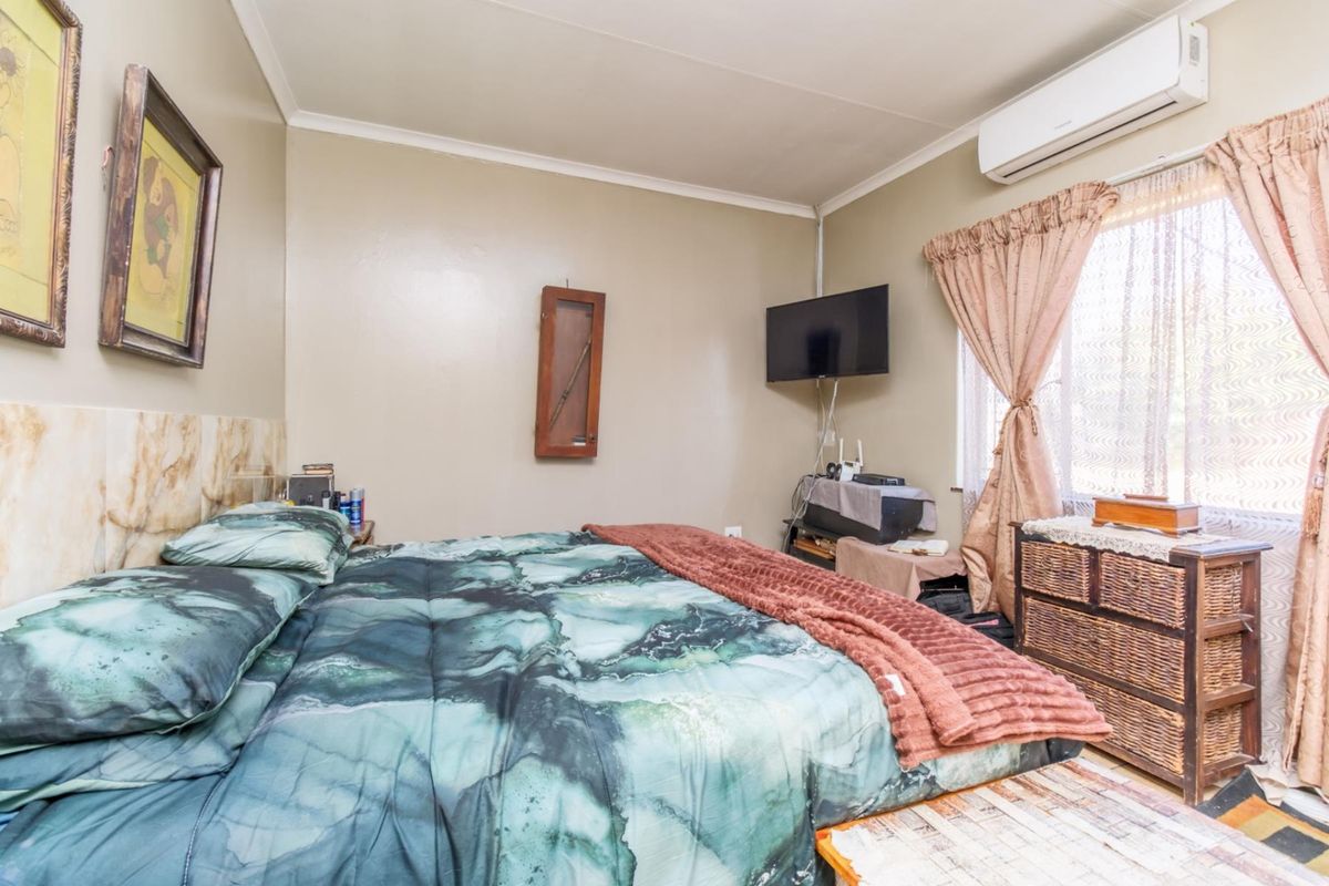 A functional bedroom featuring a wall-mounted air conditioning unit, neutral wall finishes, and a window with curtain treatments.