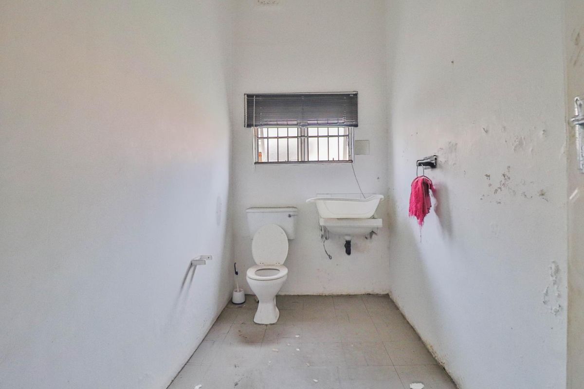 A functional bathroom featuring a standard toilet, wall-mounted basin, and security bars on the window.