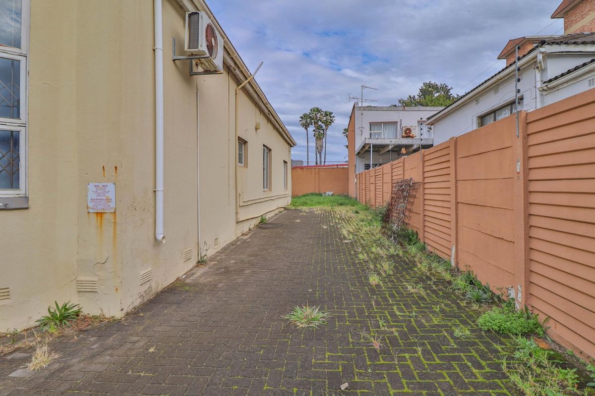 A narrow exterior side passage featuring paved flooring, boundary walling, and an external air conditioning unit mounted on the building facade.