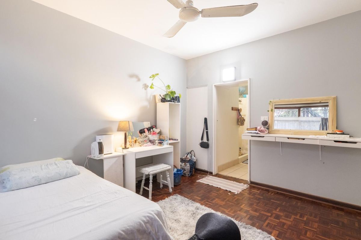 A bedroom featuring parquet flooring, a ceiling fan, and an adjoining doorway leading to a bathroom area.