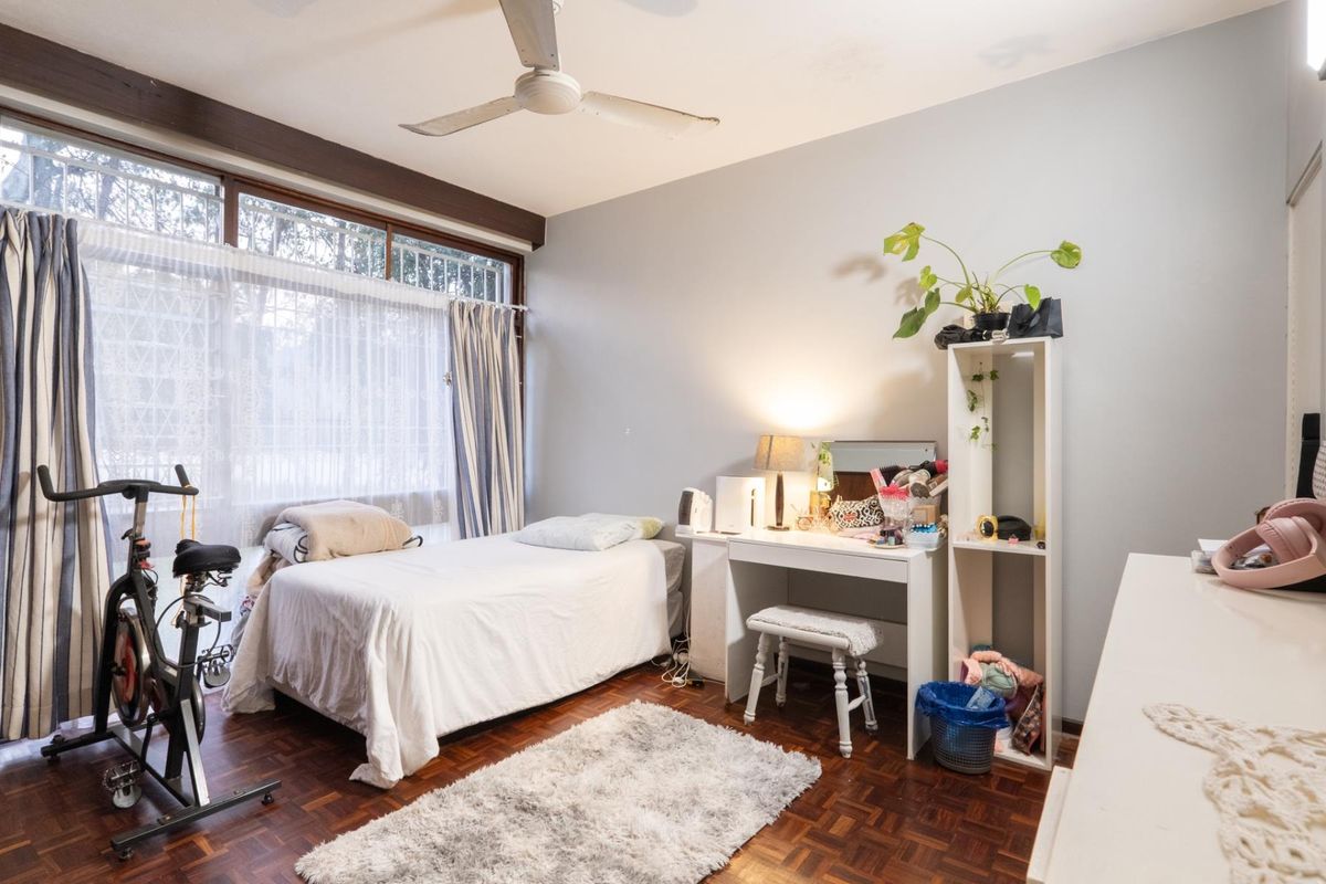 A bedroom featuring parquet flooring, a large window with natural light, and a ceiling fan.