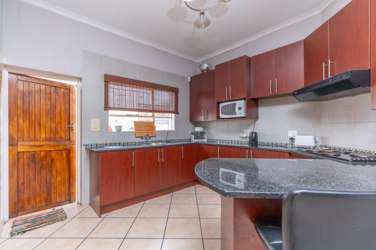 A functional kitchen featuring dark wood cabinetry, granite countertops, a built-in hob, extractor fan, and tiled flooring with direct access to the exterior.