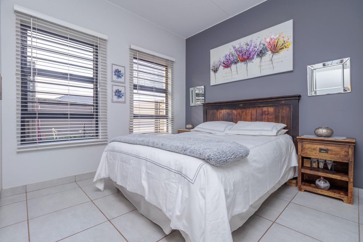 A well-maintained bedroom featuring neutral tiled flooring, dual windows with fitted blinds, and a feature wall.
