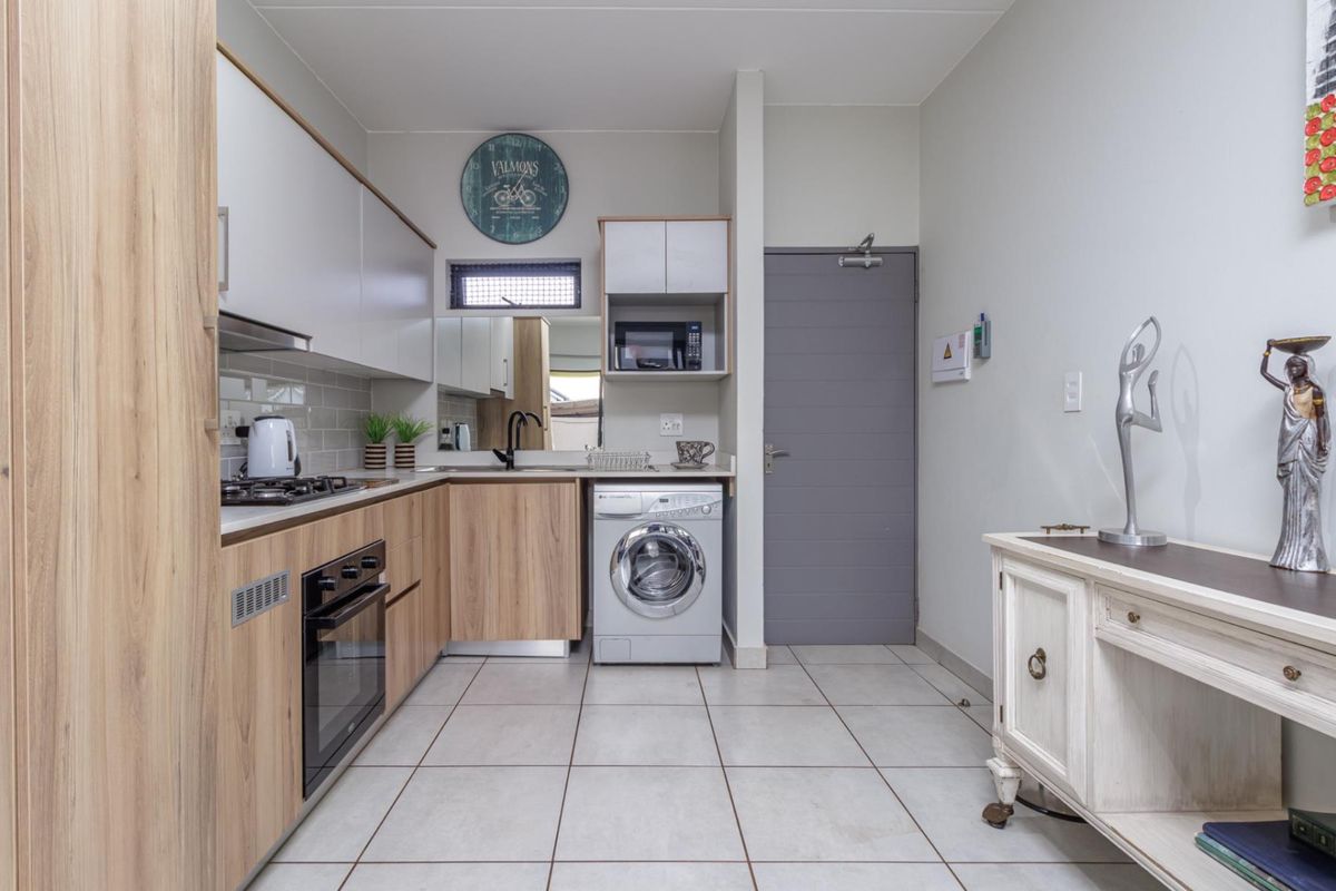 Modern kitchen featuring light wood-grain cabinetry, integrated oven and gas hob, tiled flooring, and a dedicated space for a front-loading washing machine.
