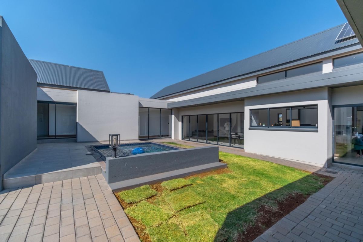 A modern courtyard featuring a small plunge pool, paved patio area, and a manicured lawn, surrounded by contemporary architectural building facades.