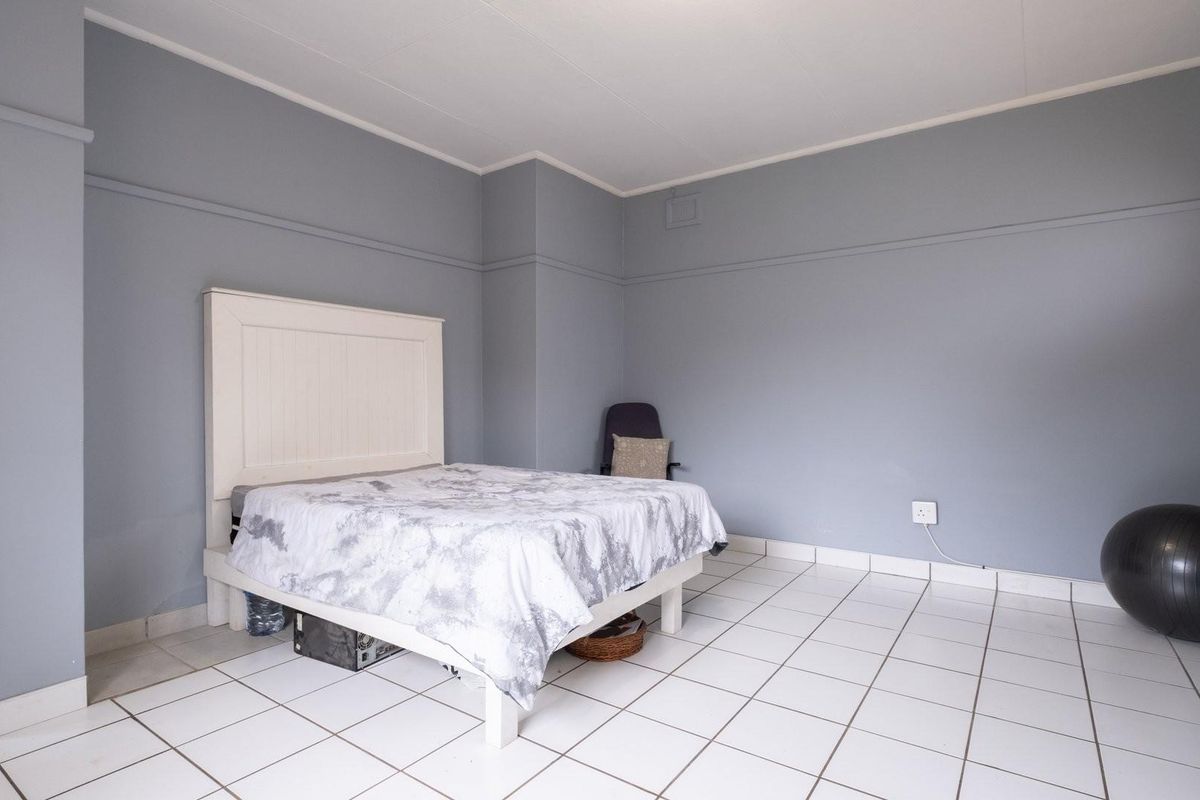 A bedroom featuring light grey walls, white tiled flooring, and a built-in wardrobe, offering a neutral space ready for personalization.