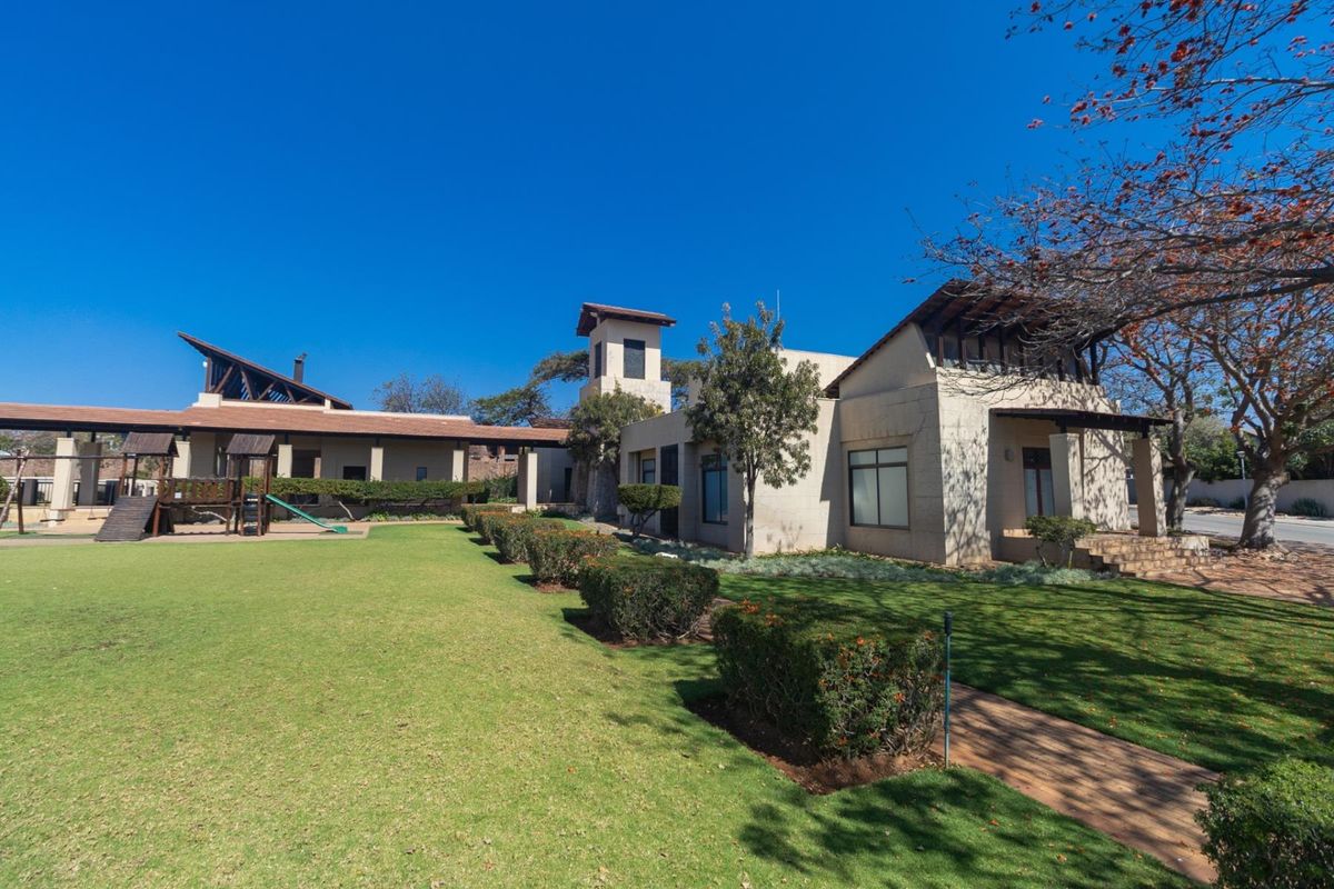A spacious rear garden featuring a well-maintained lawn, manicured hedges, and a view of the property's architectural exterior with a distinctive tower feature.