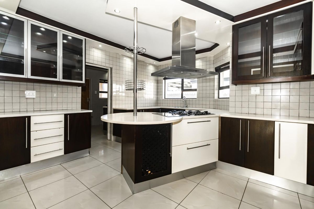 Modern kitchen featuring dark wood and white cabinetry, stone countertops, a central breakfast bar, stainless steel extractor fan, and tiled flooring.
