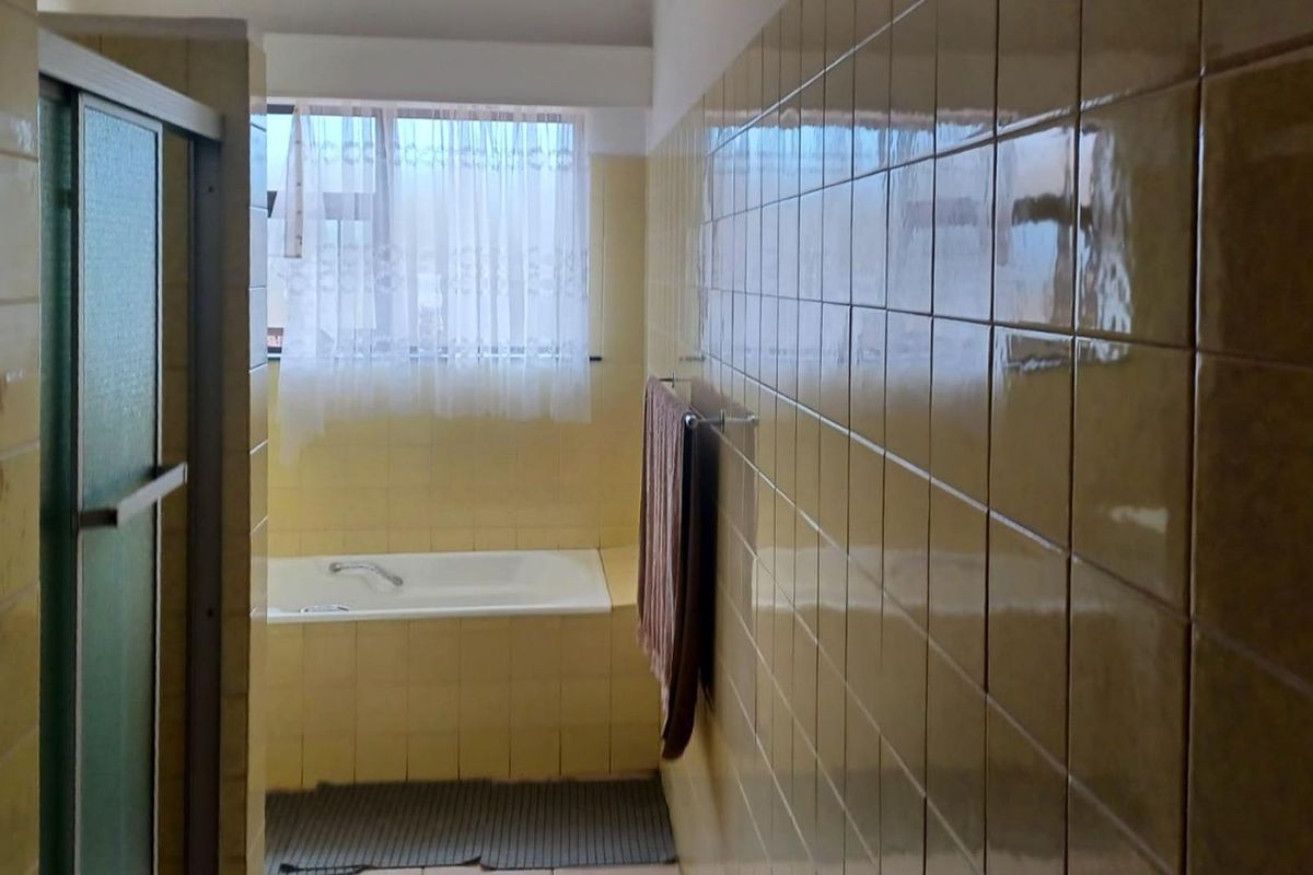 A dated bathroom featuring full-height yellow wall tiles, a built-in bathtub, and a separate shower enclosure.