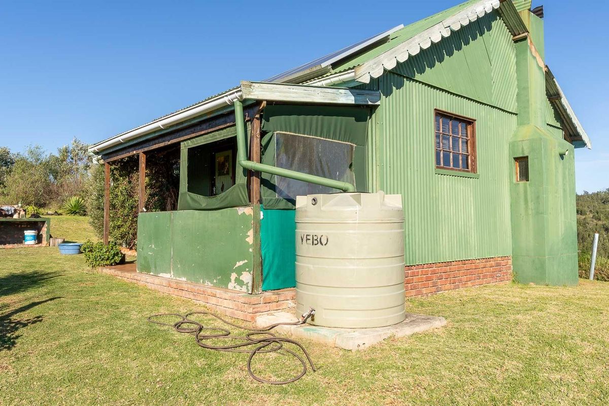Exterior view of a rustic farm cottage featuring corrugated metal cladding, a covered patio area, and an integrated rainwater collection tank.